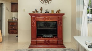 A living room with a wooden entertainment center, a flat-screen TV, and a decorative mirror on the wall. - Adorable 1Bed Cottage Walk to the Beach (St. Ann's Bay)