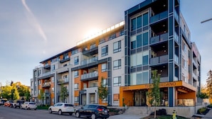 A multi-story residential building with balconies, a visible entrance, and a clear sky. - Fireplace, Courtyard, Free Heated Parking, Pets Ok (Calgary)