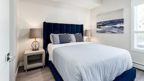 A modern bedroom with a large bed, a headboard, bedside tables, and a painting on the wall. - Fireplace, Courtyard, Free Heated Parking, Pets Ok (Calgary)