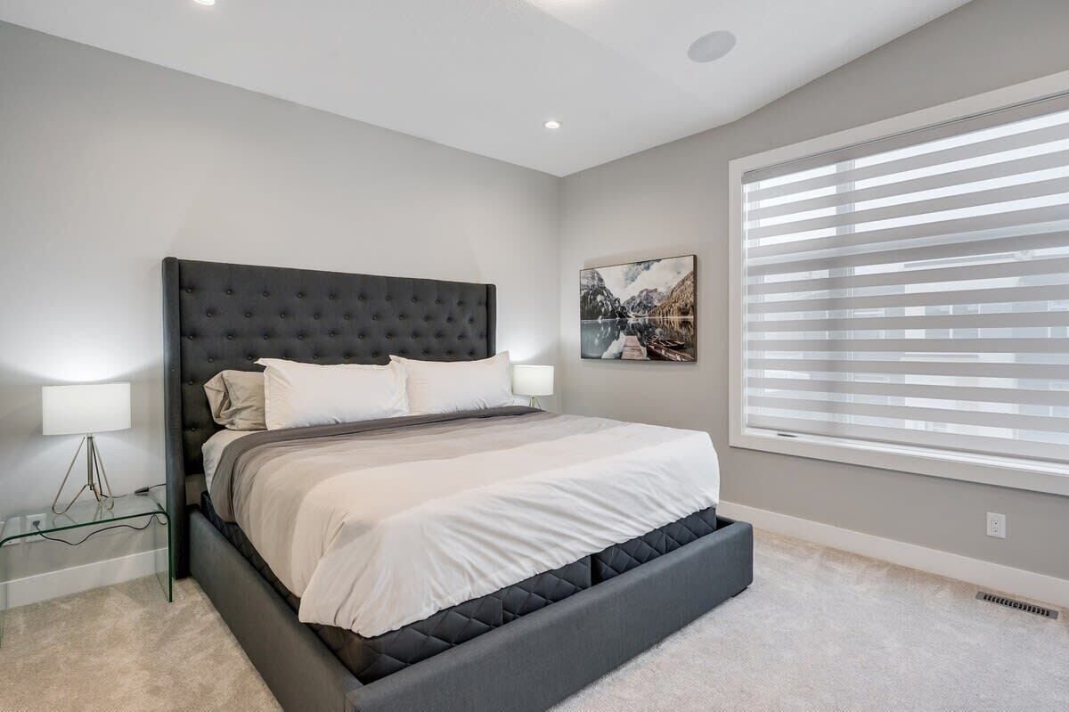 Une chambre à coucher avec un grand lit, une table de chevet, une lampe fixée au mur et une fenêtre avec des stores.