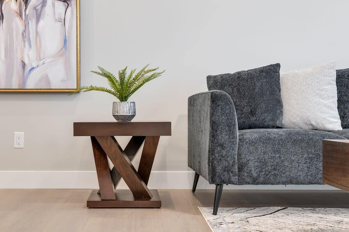 A modern living room with a grey sofa, a wooden side table with a plant, and a painting on the wall.