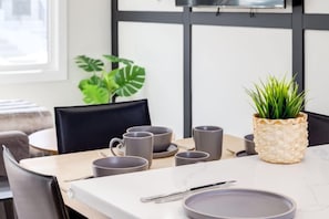 Una mesa de comedor con tazas grises, un plato y cubiertos, junto con una planta en maceta.