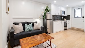 A modern living room with a black sofa, wooden coffee table, and a kitchen area with white cabinets and stainless steel appliances.