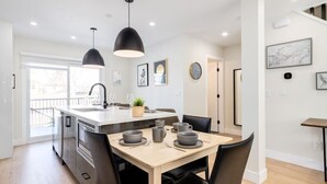 A modern kitchen with a central island, pendant lighting, and a dining area with chairs and a table. - Rare Find in Best Location, Work/Family Friendly (Calgary)