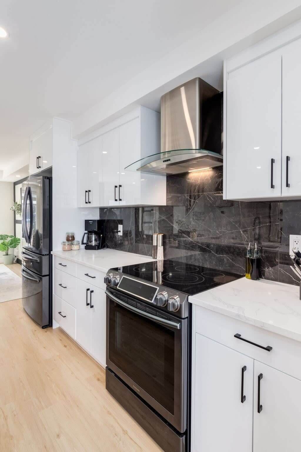 A modern kitchen with white cabinetry, a stainless steel range hood, a black stovetop, and a built-in oven.