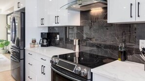 A modern kitchen with white cabinetry, a stainless steel range hood, a black stovetop, and a built-in oven.