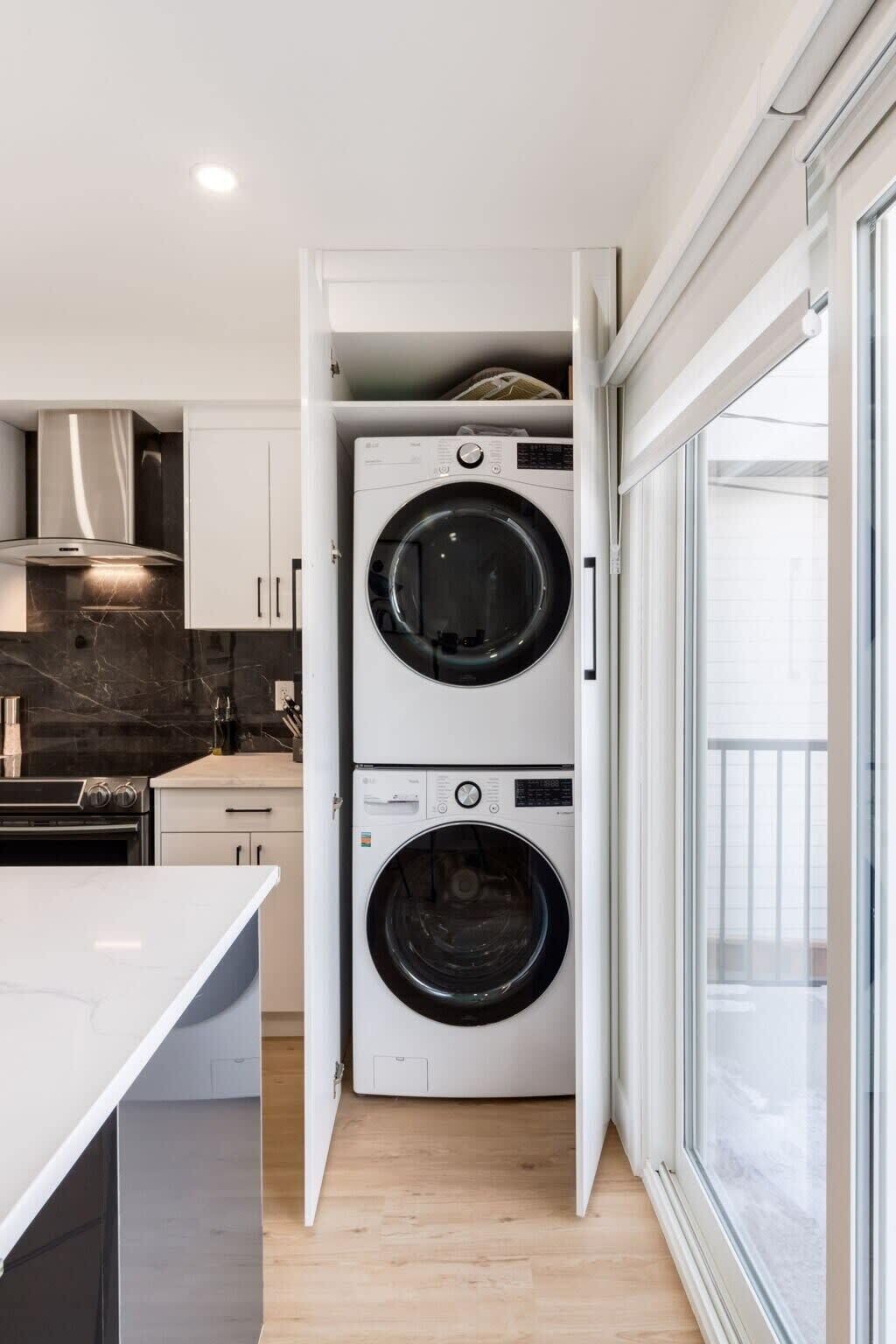 A compact kitchen with a built-in washer and dryer, a marble countertop, and a view through a glass door.