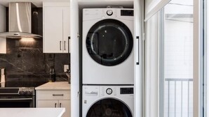 A compact kitchen with a built-in washer and dryer, a marble countertop, and a view through a glass door.