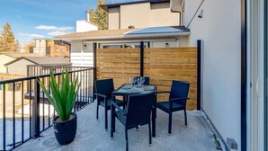 A balcony with a table and chairs, a potted plant, and a wooden fence. - Rare Find in Best Location, Work/Family Friendly (Calgary)