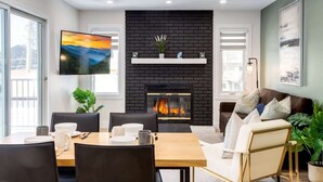 A modern living room with a fireplace, a dining area with a table and chairs, and a sofa. - Pet Friendly 4BDR w/ Main Floor office/Bed (Calgary)