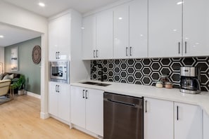 A modern kitchen with white cabinets, a microwave, a dishwasher, and a coffee maker. - Pet Friendly 4BDR w/ Main Floor office/Bed (Calgary)