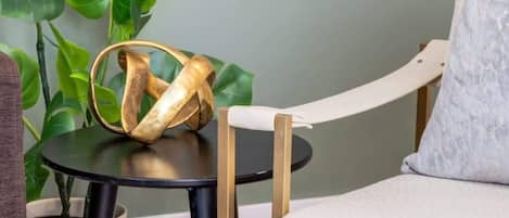 A room with a round black table, a white cushioned chair, a potted plant, and a grey wall.