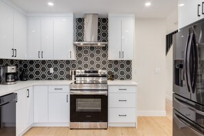 Une cuisine moderne avec des armoires blanches, une cuisinière en acier inoxydable et un dosseret à motifs noir et blanc.