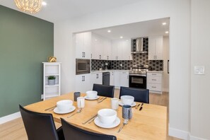 A modern kitchen with white cabinets, a black and white backsplash, and a dining area with a wooden table set for four. - Pet Friendly 4BDR w/ Main Floor office/Bed (Calgary)