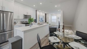 A modern kitchen with stainless steel appliances, a central island, and a dining area with a glass table and chairs.