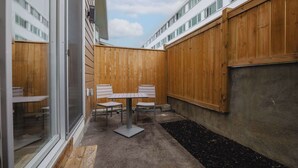 A patio with a table and chairs, surrounded by wooden fences, and a building with large windows in the background.