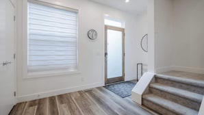 Un interior moderno con suelo de madera, un ventanal con persianas, un reloj y una escalera.