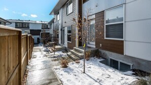 A residential building with a wooden fence, a snow-covered ground, and a small tree with yellow leaves.