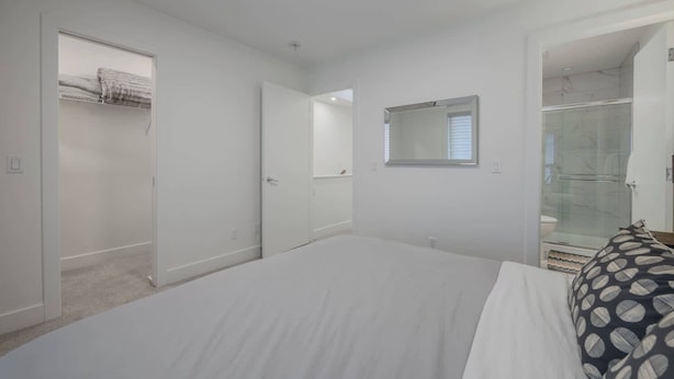 Un dormitorio con una cama grande, un vestidor, ducha con mampara de vidrio y un ventanal pequeño.