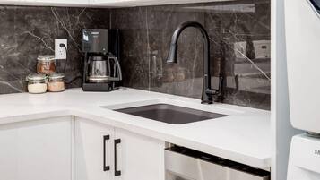 A modern kitchen with a white countertop, black faucet, and stainless steel appliances.