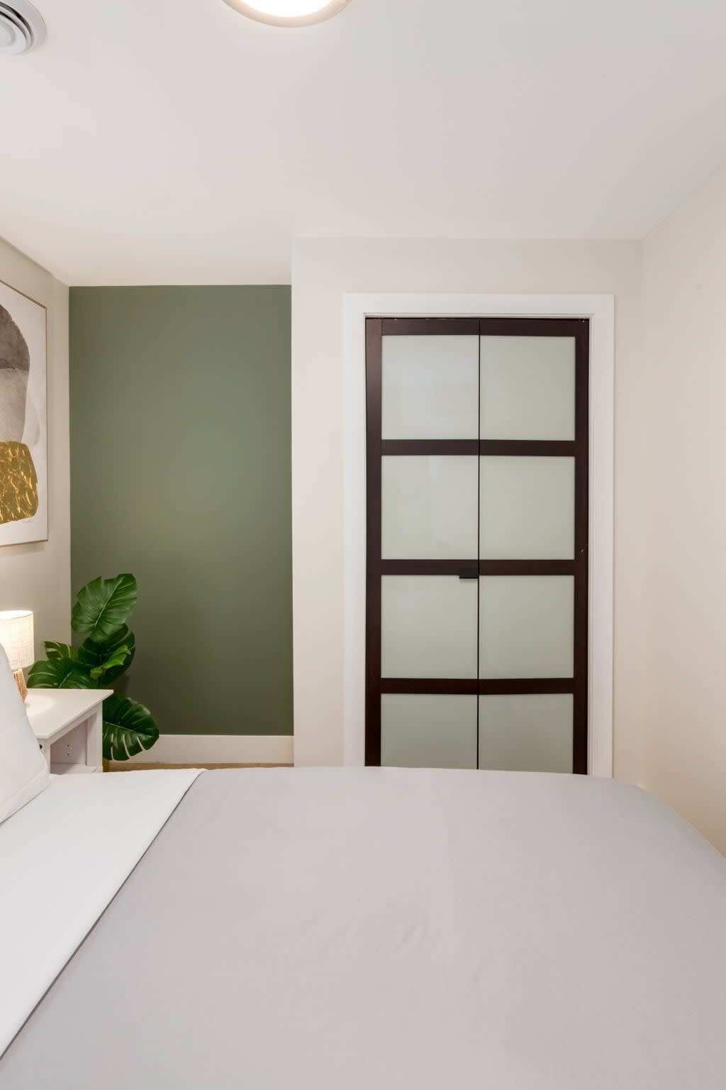 A bedroom with a bed, a nightstand, a green wall, and a door with frosted glass panels.