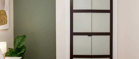 A bedroom with a bed, a nightstand, a green wall, and a door with frosted glass panels.