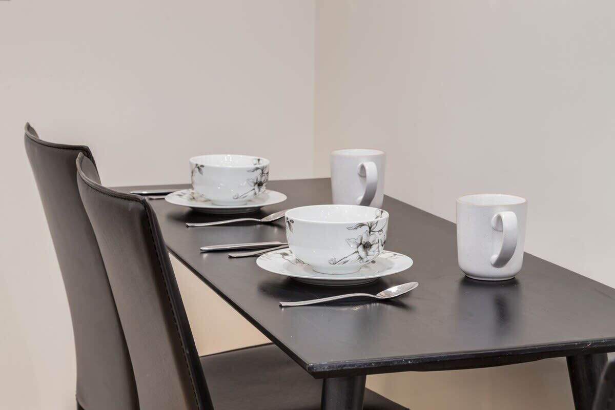 A dining table with a chair, a white cup, a white bowl, and a spoon.