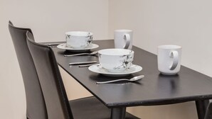 A dining table with a chair, a white cup, a white bowl, and a spoon.