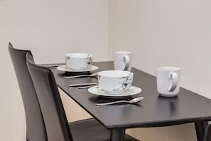 A dining table with a chair, a white cup, a white bowl, and a spoon.