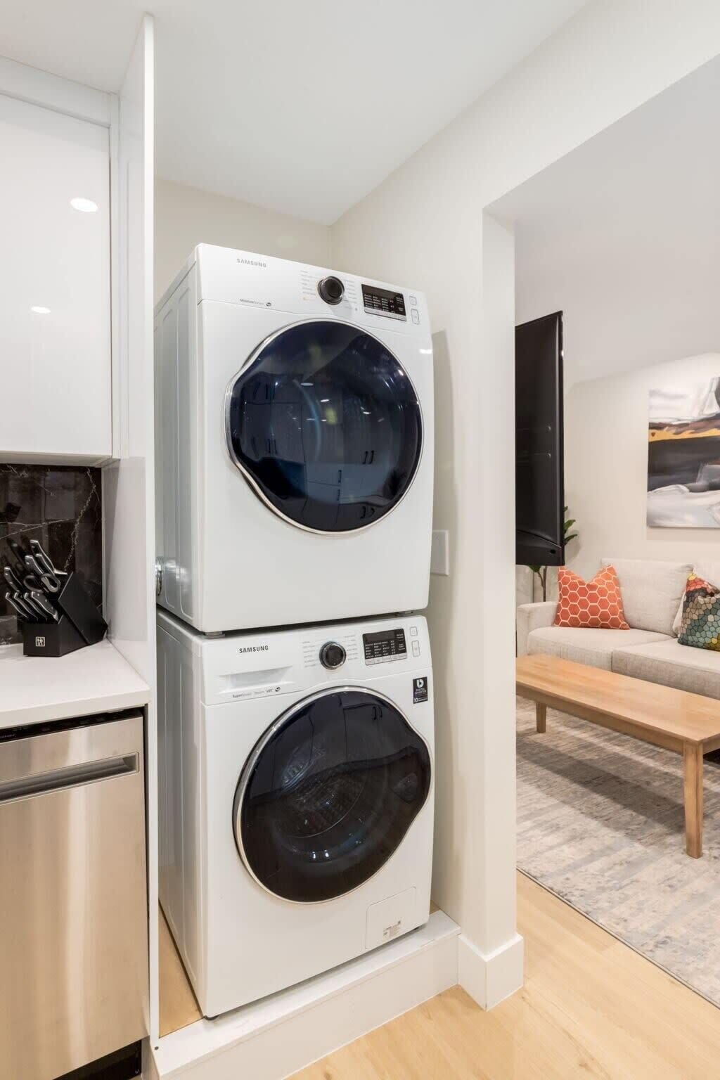 A compact laundry room with two stacked washing machines, a kitchen area with modern appliances, and a living space with a sofa and a coffee table.