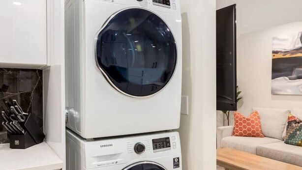 A compact laundry room with two stacked washing machines, a kitchen area with modern appliances, and a living space with a sofa and a coffee table.