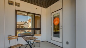 Un balcon avec une table et deux chaises, une porte avec une pancarte et une fenêtre donnant sur des immeubles.
