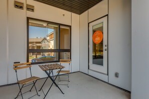 Un balcon avec une table et deux chaises, une porte avec une pancarte et une fenêtre donnant sur des immeubles.