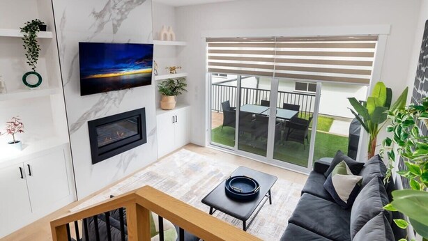 Ein modernes Wohnzimmer mit Flachbildfernseher, Kamin, einer Couch und einem Balkon mit Gartenmöbeln.