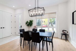 A modern dining area with a black table and chairs, a hanging light fixture, and a view of the outside through large windows.