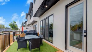 Eine moderne Terrassenausstattung im Freien mit Essplatz, Grill und einer Glastür, die auf eine Holzterrasse führt.