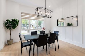 A dining area with a rectangular table, black chairs, a hanging light fixture, a potted plant, and a large mirror on the wall.