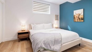 Ein Schlafzimmer mit Bett, Nachttischen, einem Fenster mit Jalousien und einem Wandbild.