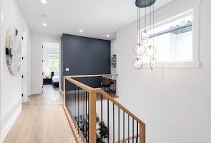 A modern interior with a wooden staircase, a dark accent wall, and a hanging light fixture.