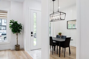 A modern dining area with a black table and chairs, a hanging light fixture, and a potted plant.