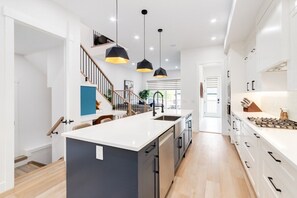 A modern kitchen with a central island, pendant lighting, and a view to the living area.