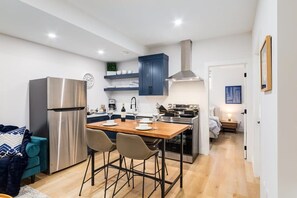 A modern kitchen with a stainless steel refrigerator, a wooden dining table with chairs, and a built-in oven.