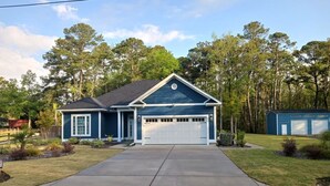 Une maison de plain-pied avec un garage, entourée d’une pelouse bien entretenue et d’arbres.