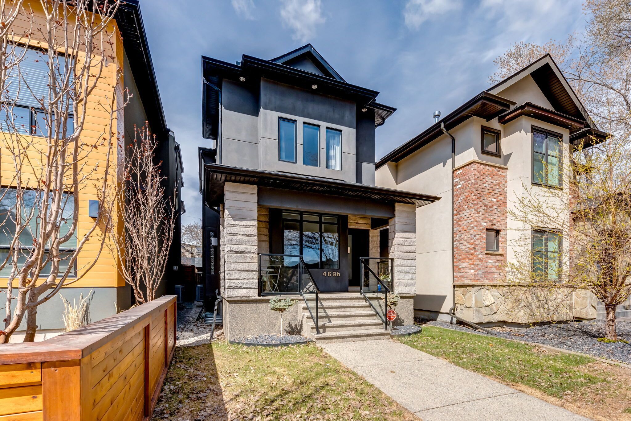 A modern two-story house with a stone facade, a wooden deck, and a clear sky.