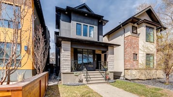 A modern two-story house with a stone facade, a wooden deck, and a clear sky.