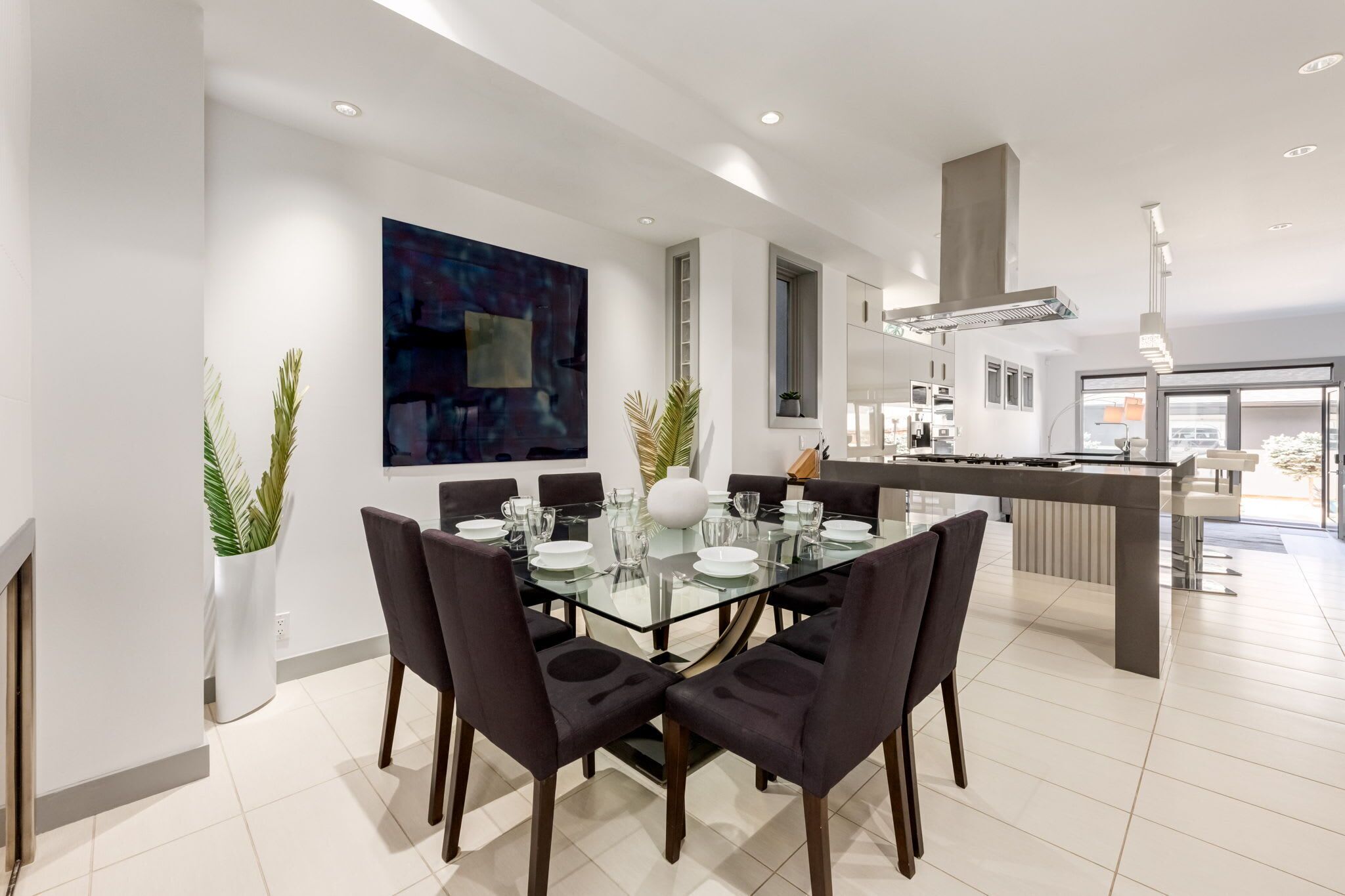 A modern dining area with a glass table, dark chairs, and a large abstract painting on the wall.