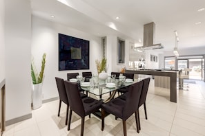 A modern dining area with a glass table, dark chairs, and a large abstract painting on the wall.