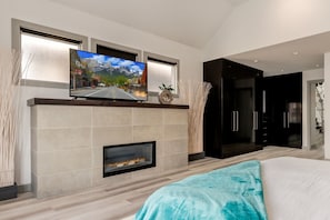 A modern bedroom with a fireplace, a TV mounted above it, and a bed with a blue blanket.
