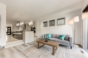 A modern living room with a sofa, coffee table, and a view into the kitchen.