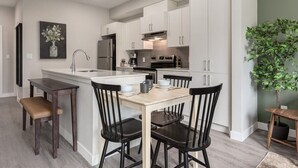 Una cocina moderna con armarios blancos, una isla central y sillas negras.
